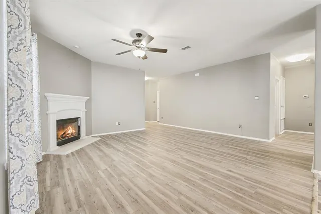 a view of an empty room with wooden floor fireplace and a window