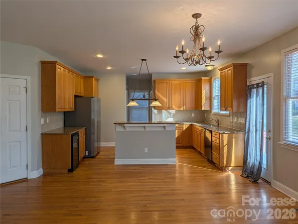 a kitchen with stainless steel appliances granite countertop a refrigerator a sink dishwasher a stove and a dining table with wooden floor
