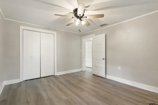 an empty room with wooden floor fan and windows