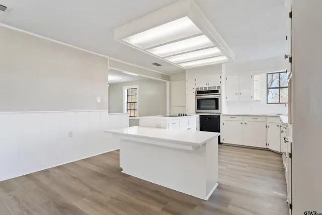 a large white kitchen with granite countertop a stove top oven a sink dishwasher and a refrigerator with wooden floor