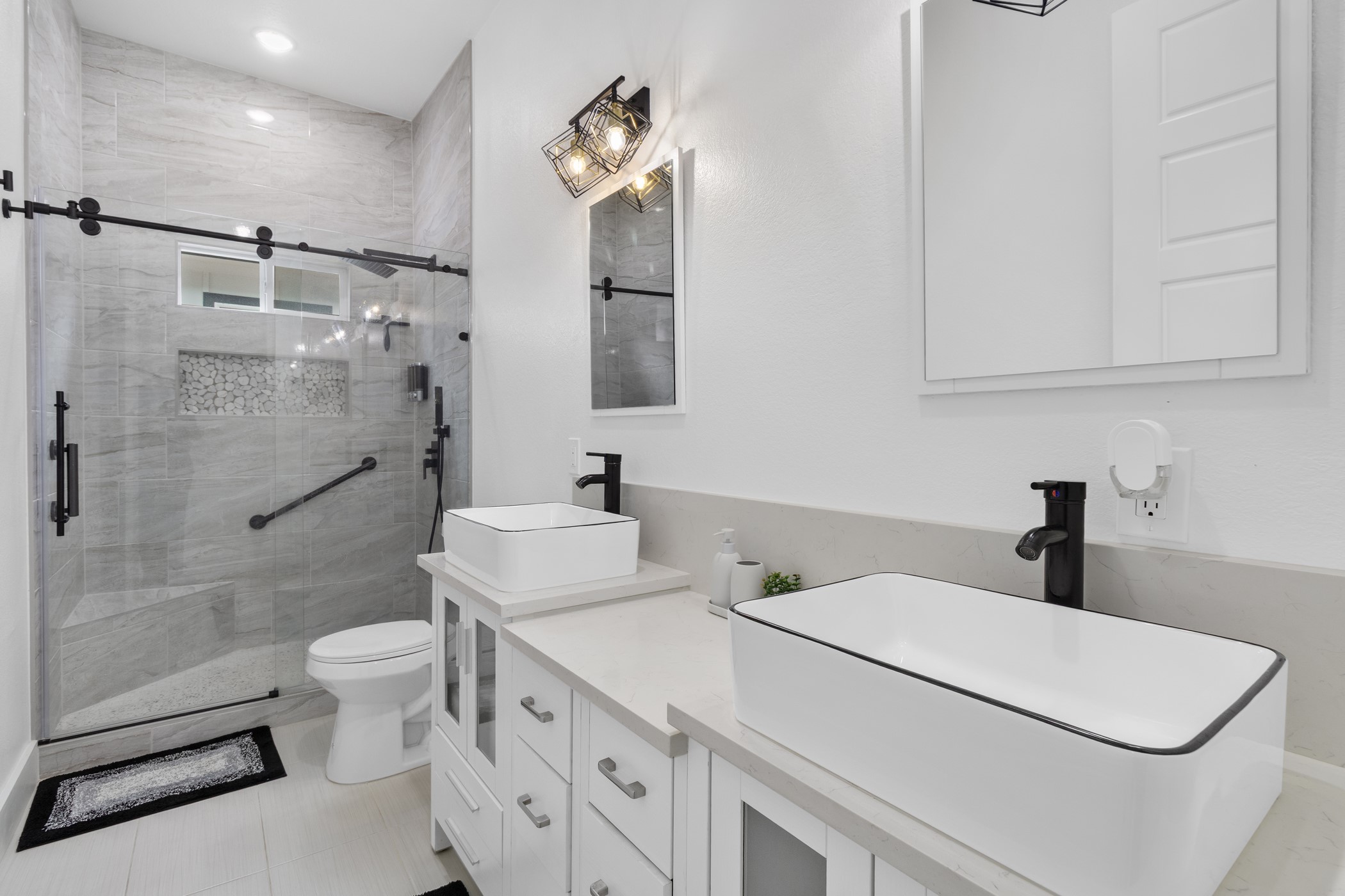 123 Zacate Street Elgin, TX 78621 - Photo 16 of 33 Contemporary bathroom featuring a dual vanity with vessel sinks and black fixtures, a glass-enclosed shower with tile surround, and light wood-finish flooring