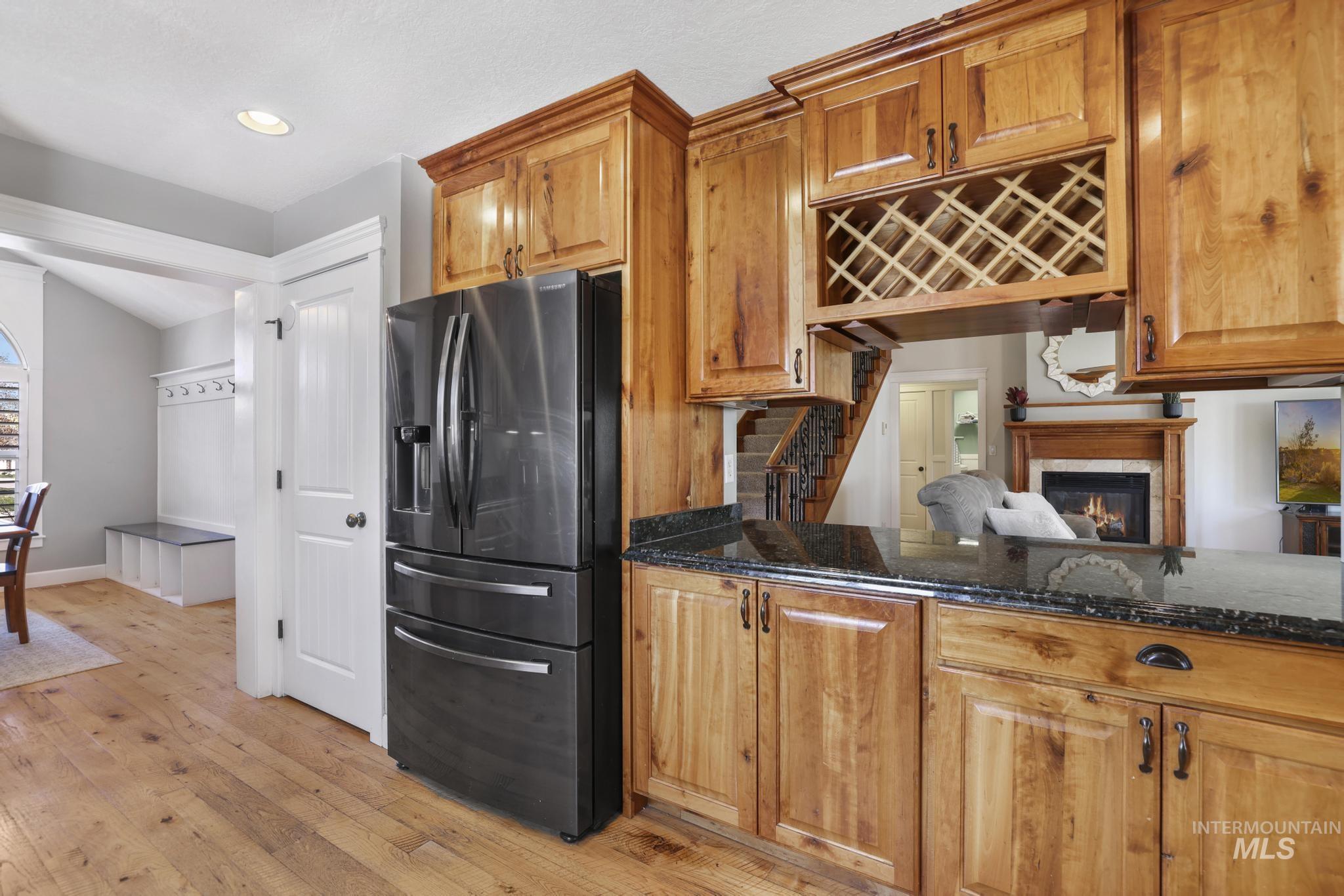 1111 Cole Street Kimberly, ID 83341 - Photo 14 of 46 Kitchen with black fridge with ice dispenser, dark stone countertops, a glass covered fireplace, light wood-style flooring, and wood finish cabinets