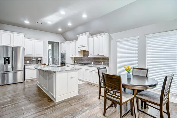 a kitchen with stainless steel appliances a stove a sink a refrigerator white cabinets and wooden floor