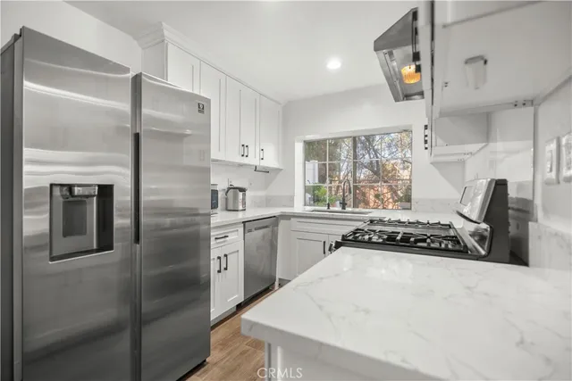 a kitchen with stainless steel appliances a refrigerator a sink and white cabinets