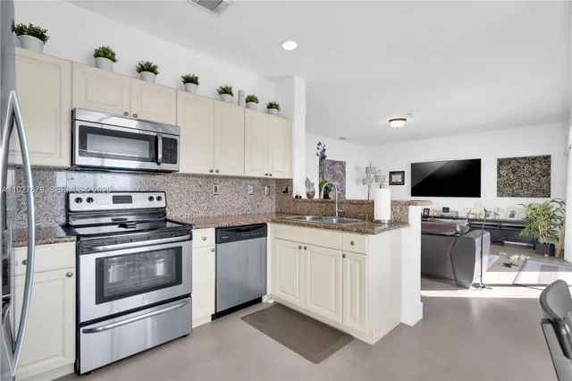 a kitchen with stainless steel appliances granite countertop a stove top oven a sink dishwasher and a microwave oven with white cabinets