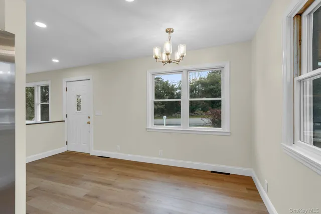 an empty room with wooden floor chandelier and windows