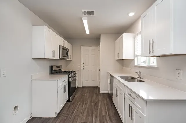 a kitchen with stainless steel appliances a sink dishwasher a stove top oven a refrigerator with white cabinets and wooden floor