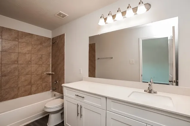 a bathroom with a bathtub shower sink vanity mirror and toilet