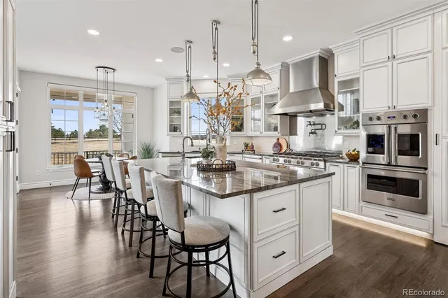 a kitchen with stainless steel appliances kitchen island granite countertop a dining table chairs and white cabinets