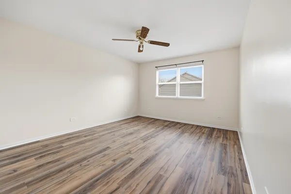 an empty room with wooden floor ceiling fan and windows