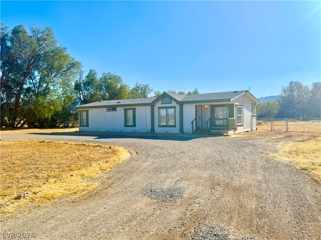 6450 Vicki Ann Road Pahrump, NV 89048 - Photo 1 of 9 A welcoming home with a long gravel driveway leads to a cozy front porch, surrounded by mature trees.