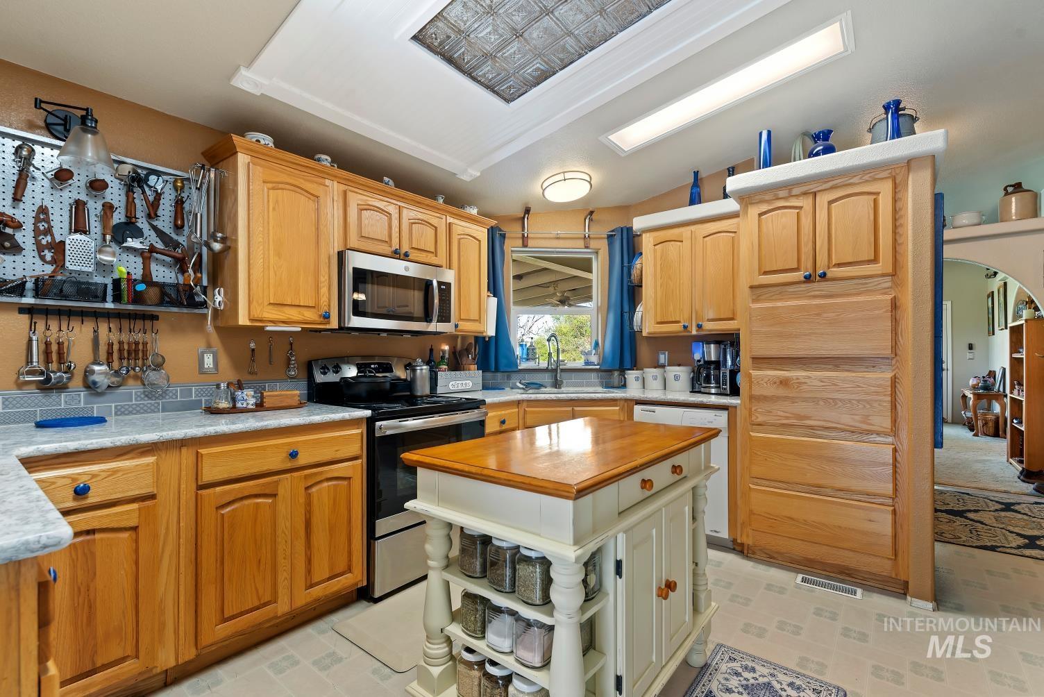 19152 Marsing Road Caldwell, ID 83607 - Photo 20 of 47 Kitchen featuring wood cabinetry, light-toned countertops, a stainless steel microwave, a built-in pantry with vertical paneling, and a central island with a wood top