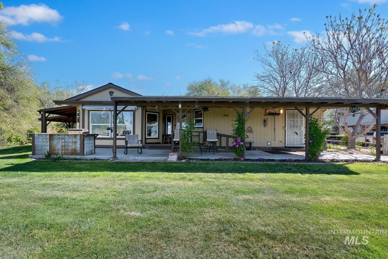 19152 Marsing Road Caldwell, ID 83607 - Photo 2 of 47 Expansive green lawn with a single-story residence featuring a covered concrete patio, a built-in outdoor bar with a rustic corrugated metal finish, multiple windows, and a security screen door