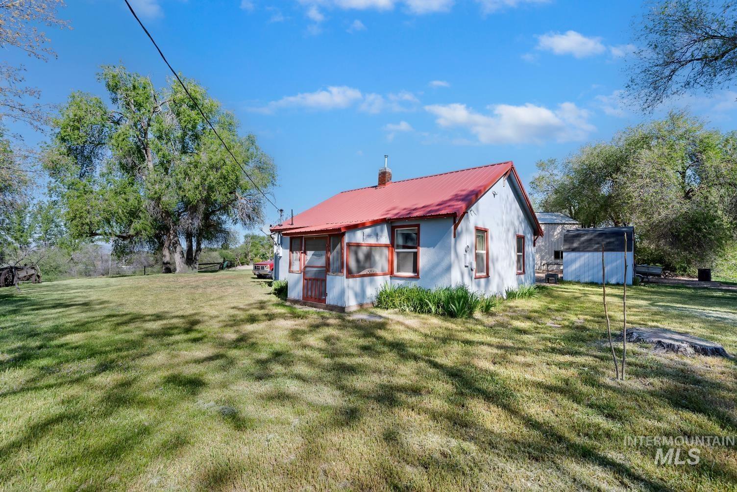 19152 Marsing Road Caldwell, ID 83607 - Photo 37 of 47 Light blue exterior with a red metal roof, featuring a screened-in porch with a wooden door
