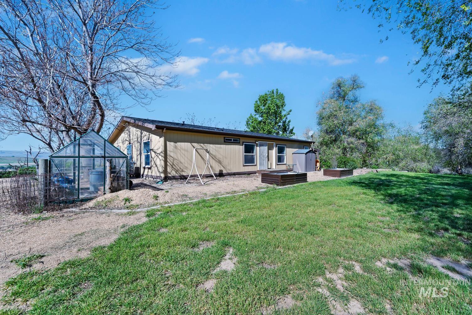 19152 Marsing Road Caldwell, ID 83607 - Photo 10 of 47 Expansive grassy yard area featuring a detached greenhouse, multiple raised garden beds, and a storage shed