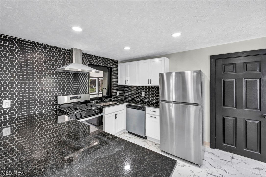 7339 River Road Olmsted Falls, OH 44138 - Photo 11 of 45 Kitchen featuring black honeycomb tile backsplash, stainless steel appliances, white cabinetry, dark granite countertops, and recessed lighting