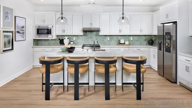 a kitchen with stainless steel appliances granite countertop a stove a sink a microwave a refrigerator and white cabinets with wooden floor