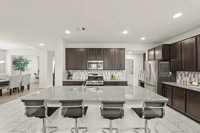 a kitchen with stainless steel appliances kitchen island granite countertop a dining table chairs refrigerator and cabinets
