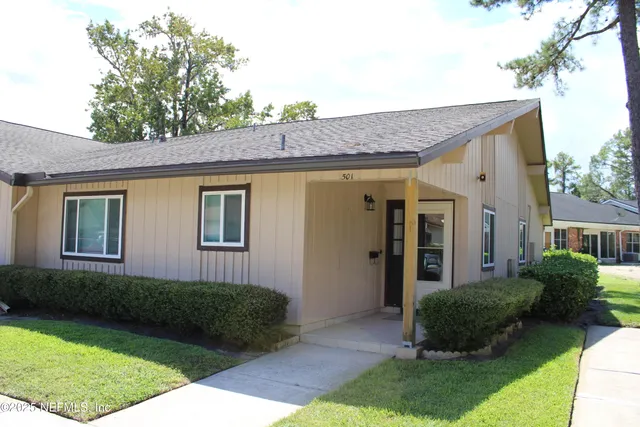 a view of a house with a yard plants and large tree