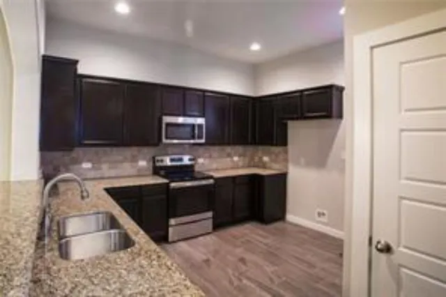 a kitchen with stainless steel appliances granite countertop a stove a sink and a refrigerator with wooden floor