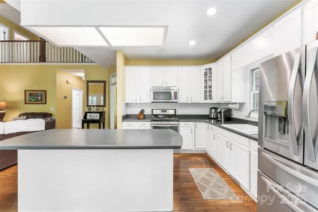 a kitchen with stainless steel appliances granite countertop a refrigerator a sink dishwasher a stove and white countertops with wooden floor