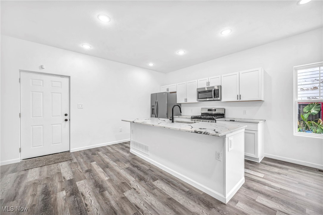 3709 Sudbury Road Cleveland, OH 44120 - Photo 9 of 29 Kitchen featuring white cabinetry, light hardwood / wood-style flooring, an island with sink, light stone countertops, and appliances with stainless steel finishes