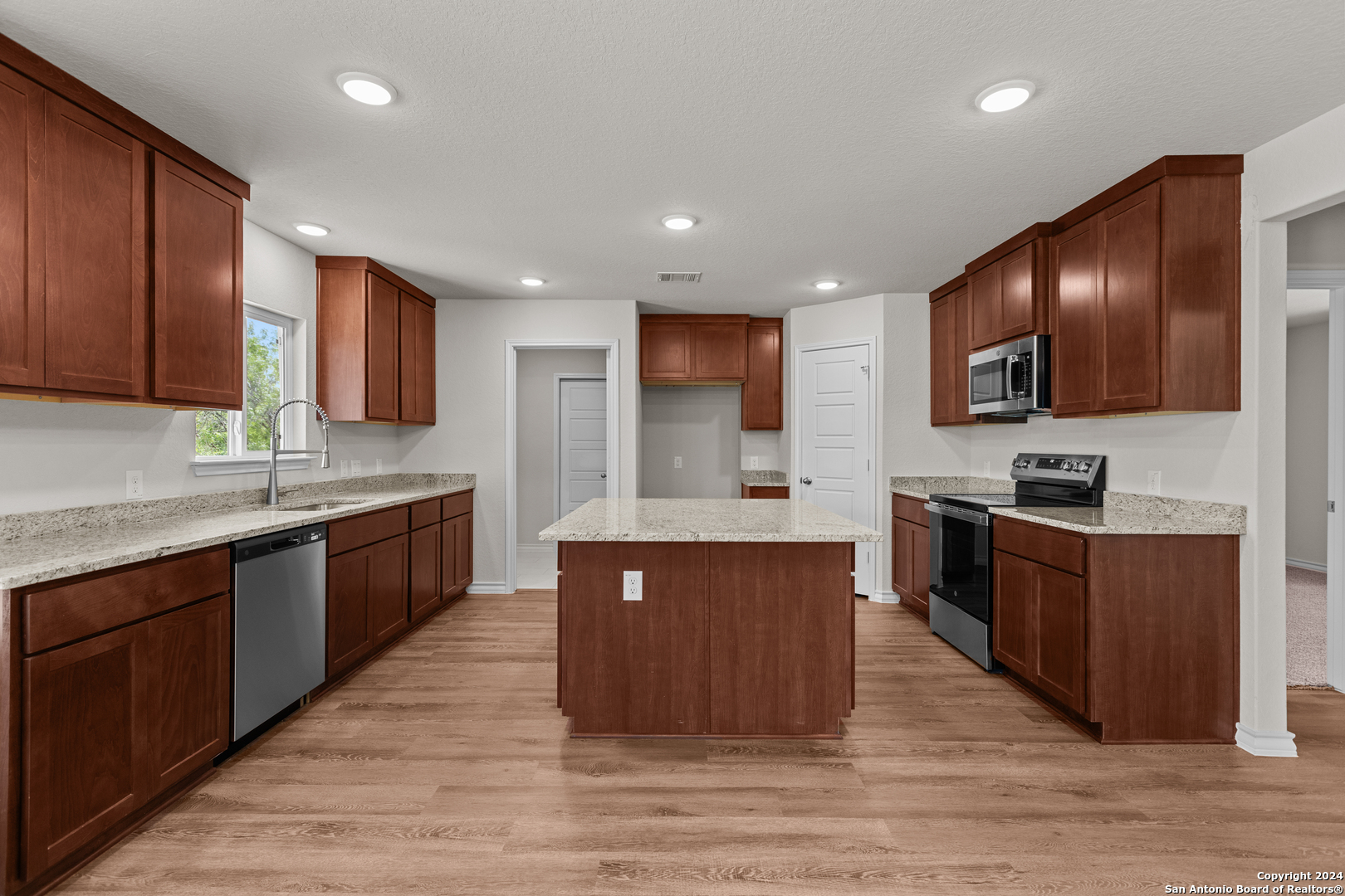 117 Sylas Hayes Loop Pleasanton, TX 78064 - Photo 23 of 38 a large kitchen with stainless steel appliances wooden cabinets a stove a sink and a wooden floors