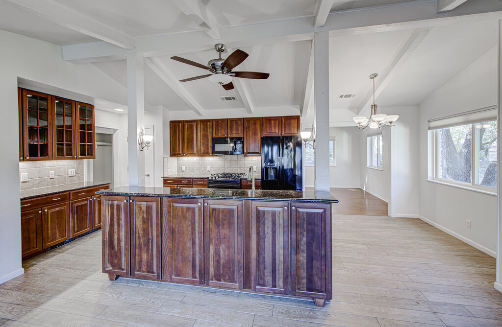 2400 Spring Creek Drive Austin, TX 78704 - Photo 8 of 38 Kitchen featuring dark stone countertops, suspended lighting, glass insert cabinets, vaulted ceiling with beams, and ceiling fan