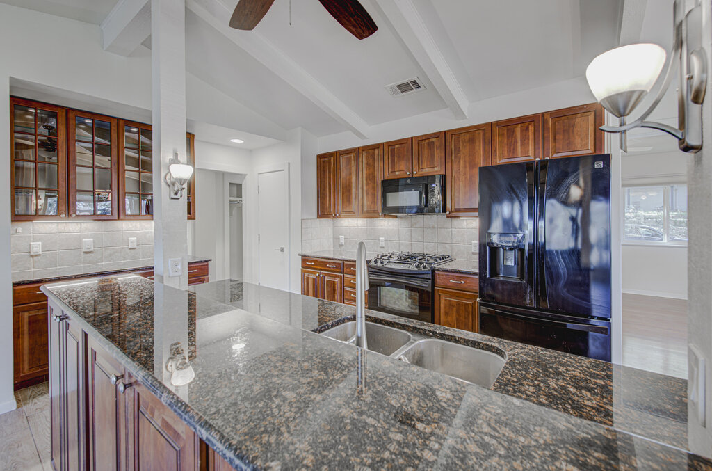 2400 Spring Creek Drive Austin, TX 78704 - Photo 9 of 38 Kitchen featuring black appliances, wood finish cabinetry, dark stone countertops, and vaulted ceiling with beams