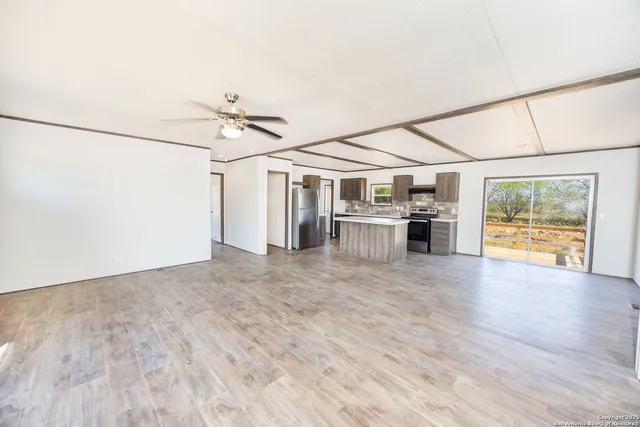 an empty room with wooden floor ceiling fan and windows