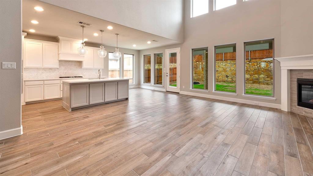 4237 Capstone Road Midlothian, TX 76065 - Photo 3 of 25 Open-concept living space featuring wood-finish flooring, a contemporary kitchen island with pendant lighting, a tile-surround fireplace, and expansive windows