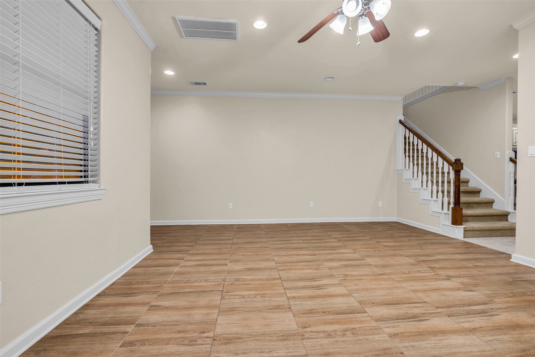 1898 Longmire Road, Unit 5 Conroe, TX 77304 - Photo 15 of 48 This spacious living area features modern tile flooring, neutral walls, and a ceiling fan. It offers natural light from a large window with blinds and includes a staircase with wooden railings, leading to the upper level. Perfect for a cozy and inviting atmosphere.