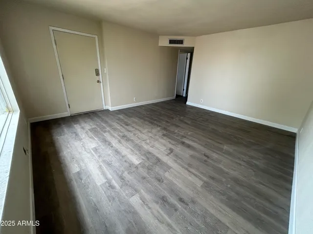 a view of an empty room with wooden floor and a window
