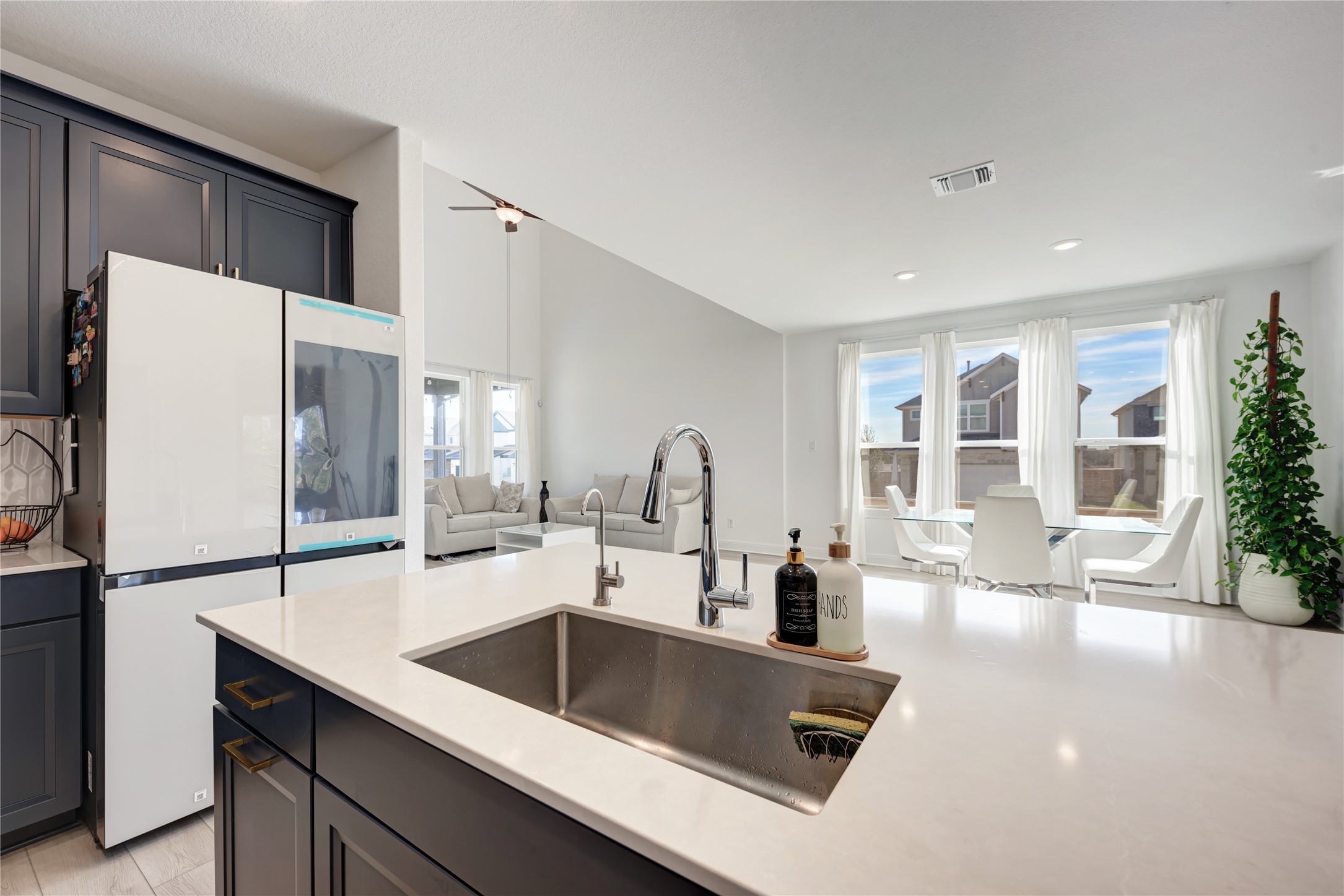 316 Regatta Trail Leander, TX 78641 - Photo 10 of 39 Open-concept interior featuring a large kitchen island with an undermount sink, dark cabinetry with brass hardware, vaulted ceilings in the living area, and multiple windows providing ample ambient light