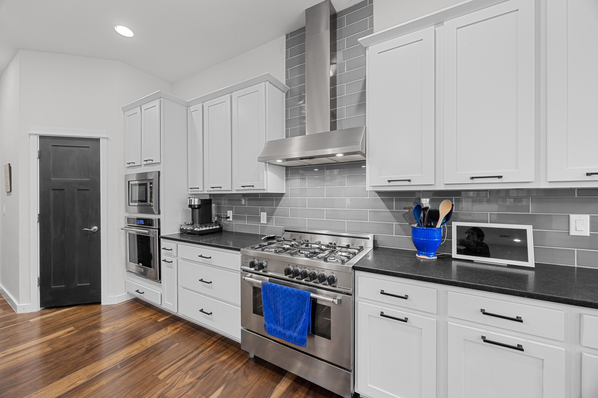 3907 Becker Avenue Austin, TX 78751 - Photo 11 of 37 Open kitchen with stainless steel appliances, white cabinets, wood flooring, backsplash, and recessed lighting.