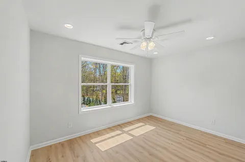 an empty room with wooden floor ceiling fan and windows