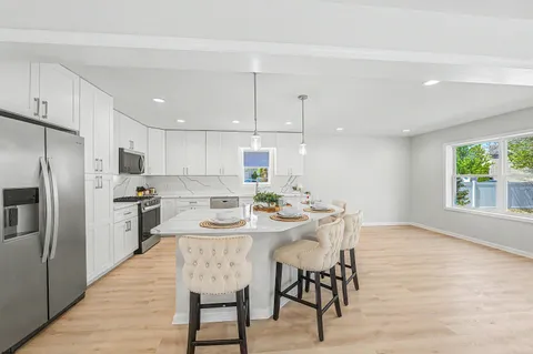 a kitchen with stainless steel appliances kitchen island granite countertop a dining table chairs refrigerator and sink