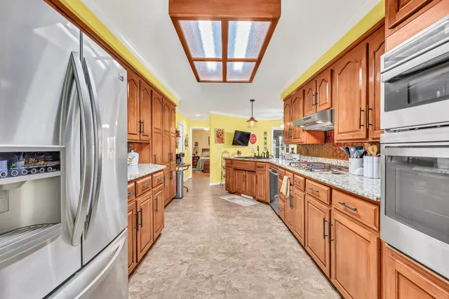 a kitchen with stainless steel appliances granite countertop a refrigerator a sink dishwasher a stove and a dining table with wooden floor