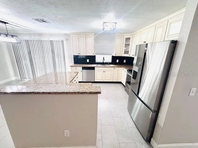 a kitchen with granite countertop a refrigerator a sink and white cabinets