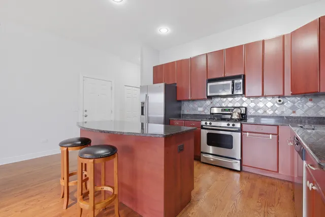 a kitchen with stainless steel appliances granite countertop a sink a stove a refrigerator cabinets and wooden floor