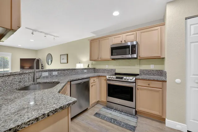 a kitchen with stainless steel appliances granite countertop a refrigerator a stove and a sink with wooden floor