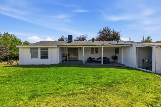 4270 River Road Oakley, UT 84055 - Photo 39 of 46 Spacious rear yard featuring a covered patio, sliding glass door access, white vertical siding, multiple windows, and an attached covered storage area