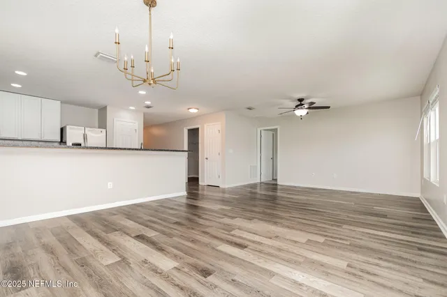 a view of an empty room with kitchen view and a chandelier