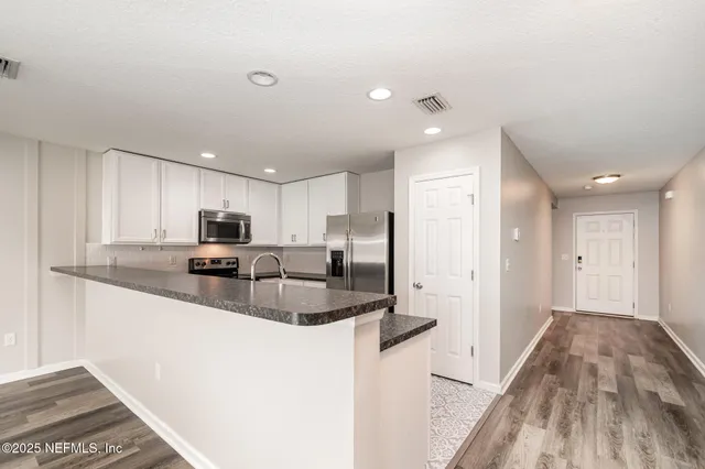 a kitchen with stainless steel appliances granite countertop a refrigerator a sink a stove and white cabinets with wooden floor