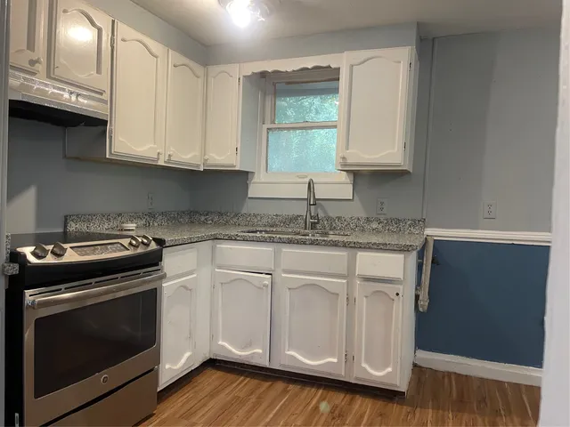 a kitchen with granite countertop white cabinets and a stove with wooden floor