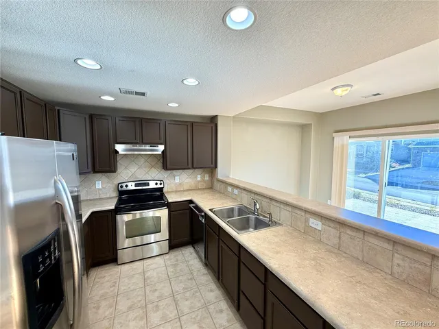 a kitchen with stainless steel appliances granite countertop a sink stove refrigerator and cabinets