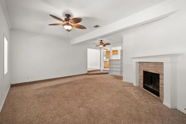 a view of an empty room with chandelier fan and fire place