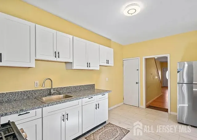 a kitchen with stainless steel appliances granite countertop a refrigerator a sink and white cabinets