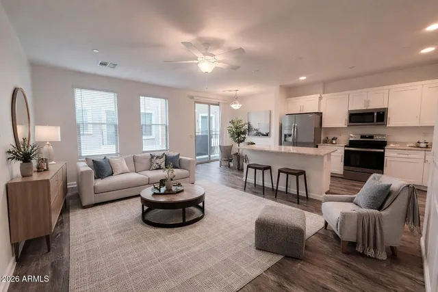a living room with furniture a rug kitchen view and a large window
