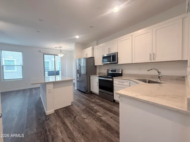 a kitchen with granite countertop a stove top oven a sink a refrigerator white cabinets and wooden floor